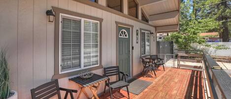 A covered outdoor area with wooden benches and tables, a green door, and a window with blinds.