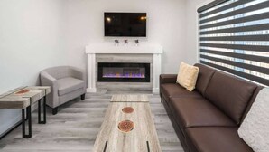 A modern living room with a fireplace, a sofa, a coffee table, and a TV mounted on the wall.