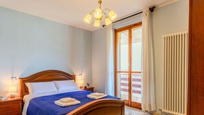 Un dormitorio con cama de madera, una mesita de noche, una lámpara, un radiador y un ventanal corredero a un balcón.