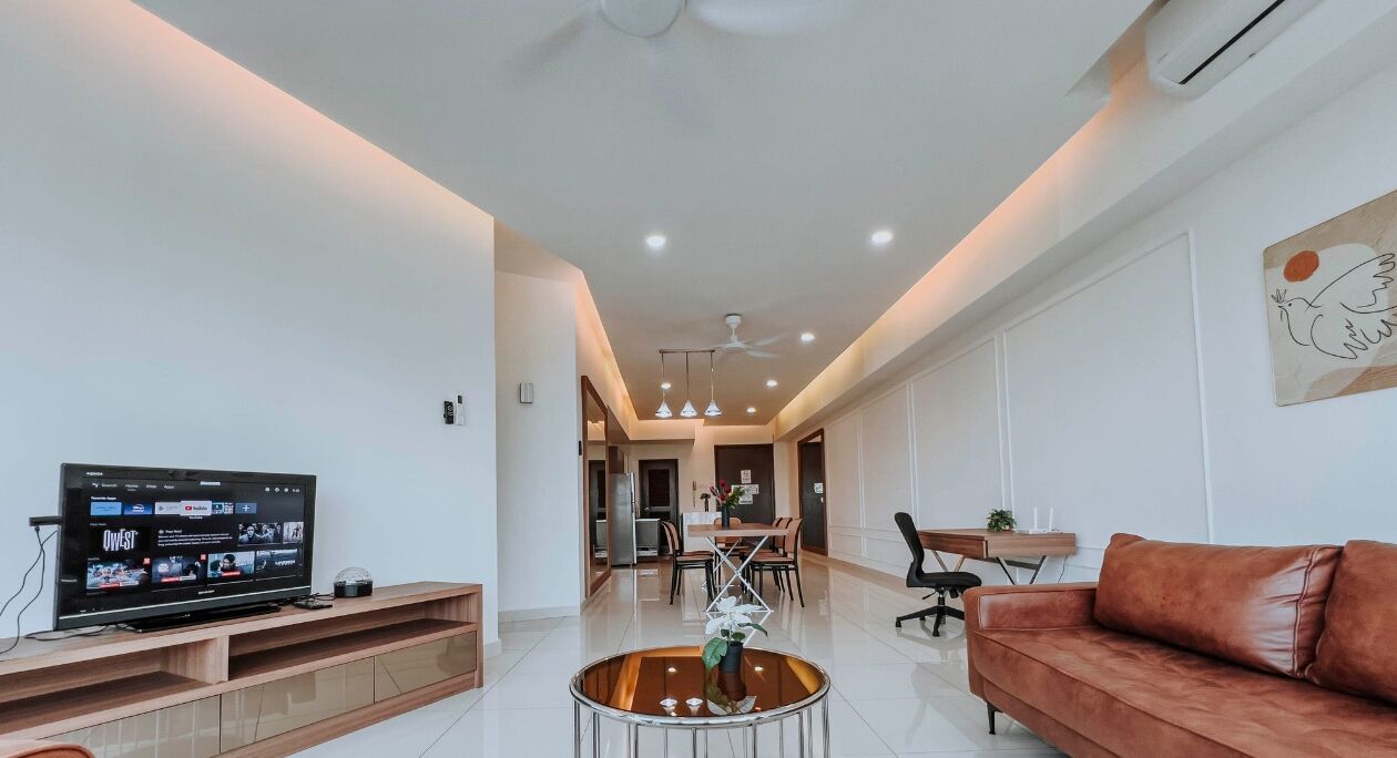 A modern living room with a flat-screen TV, a leather sofa, a coffee table, and a dining area with chairs and a table.