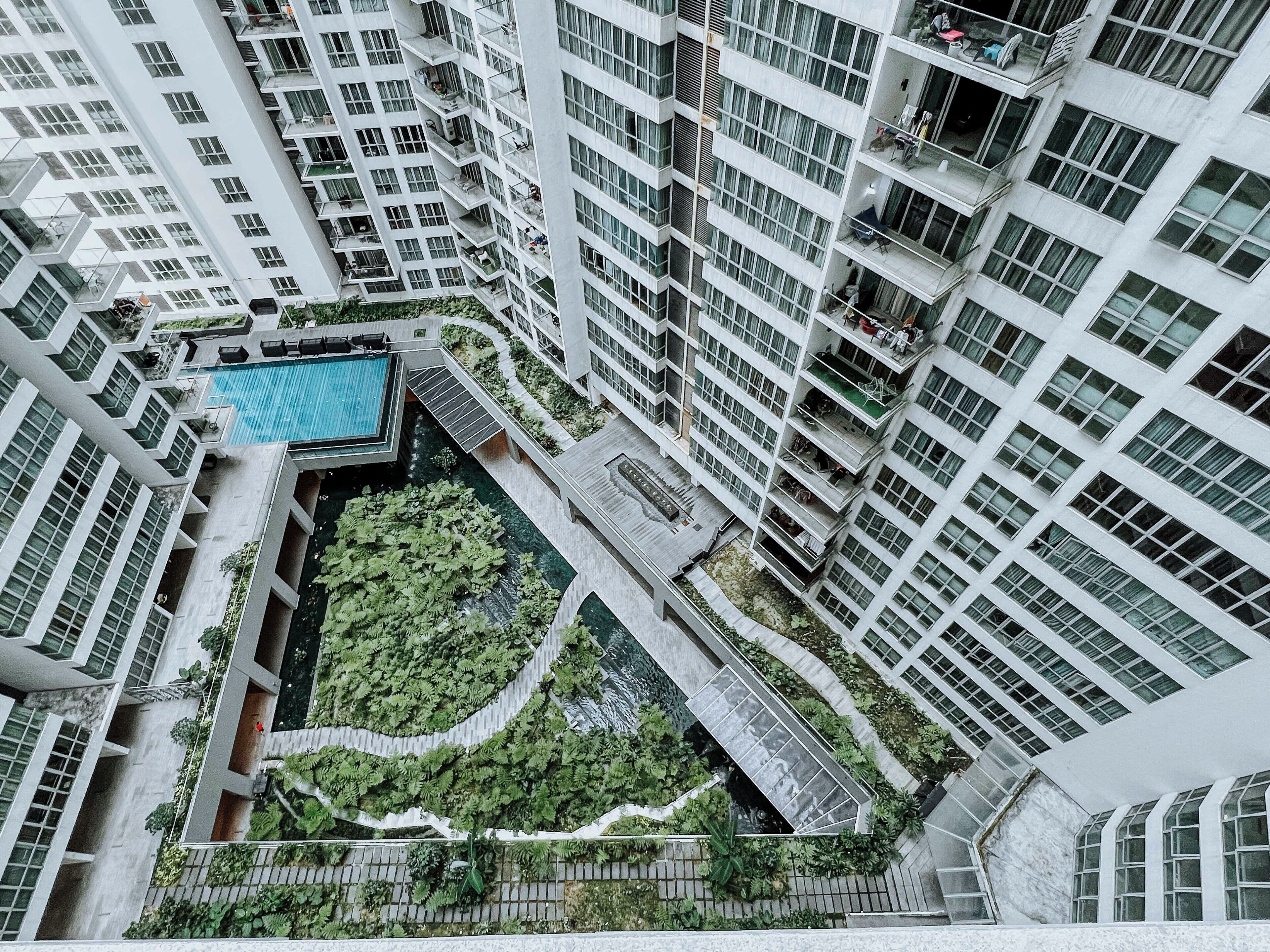 A high-rise building with multiple balconies, a central courtyard with a swimming pool, and surrounding greenery.