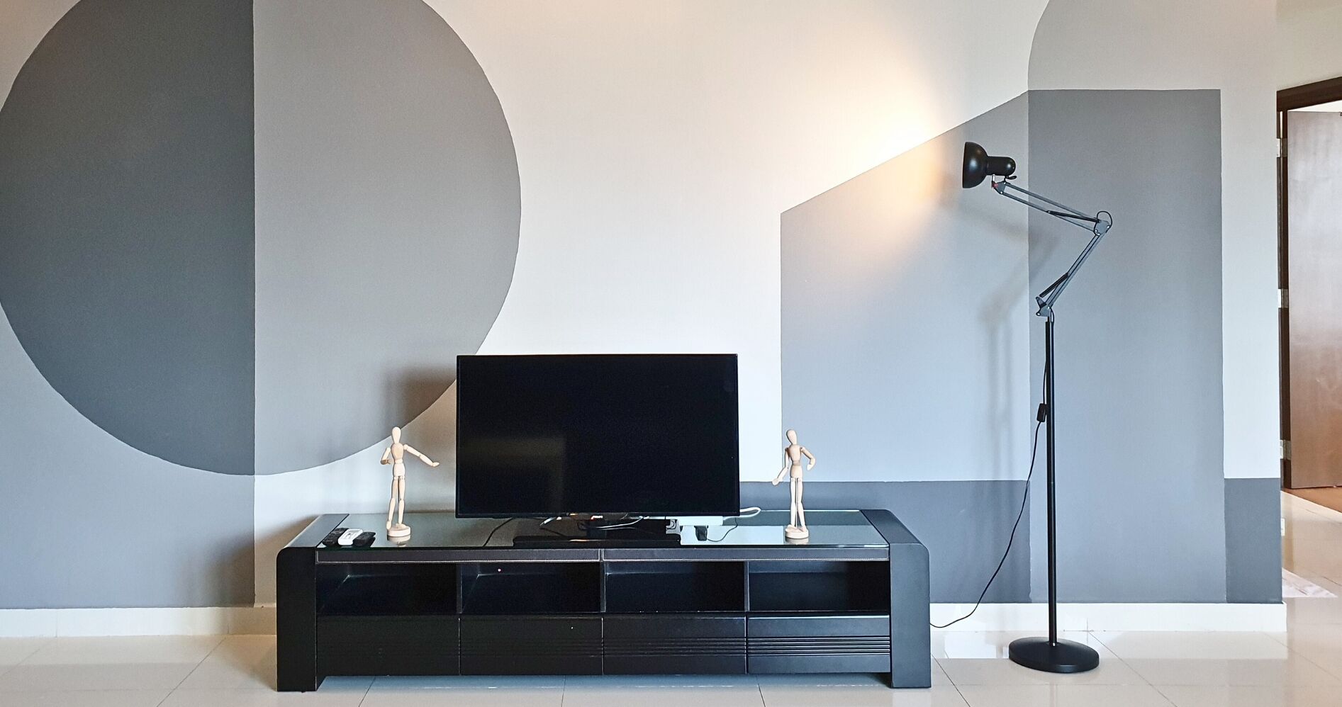 A modern living room with a flat-screen TV on a black entertainment unit, a floor lamp, and two white figurines.