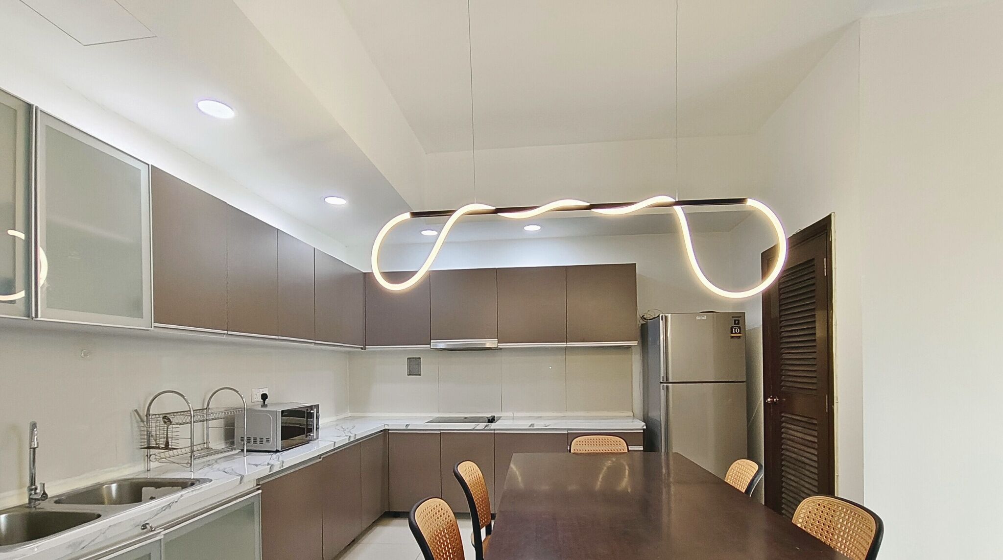 A modern kitchen with a dining area, featuring a central island, built-in appliances, and a unique ceiling light design.