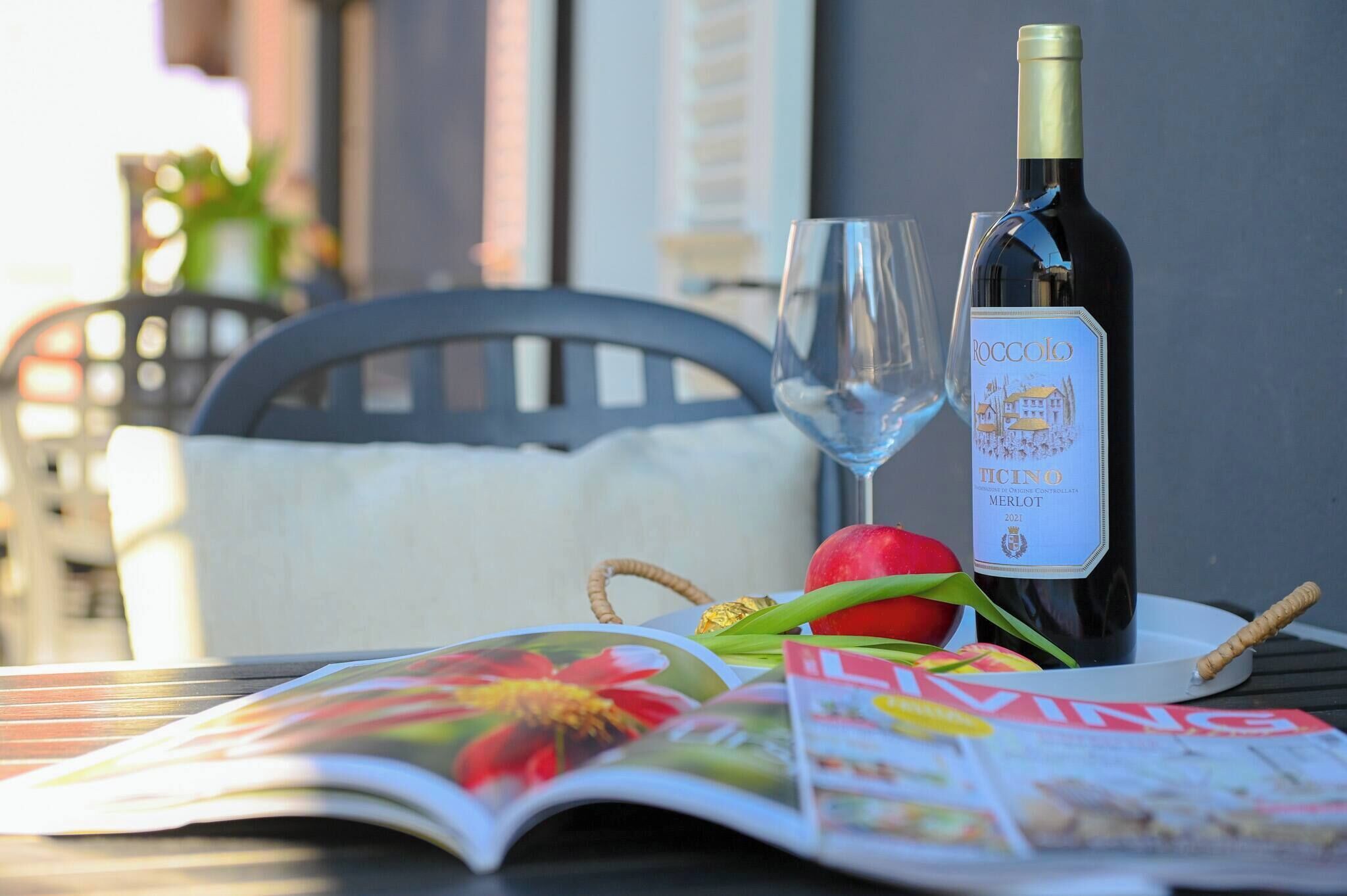 A bottle of wine, a glass, a red apple, and a magazine on a table.