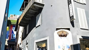 A building with a private terrace indicated by a yellow arrow, a storefront with mannequins, and a clear blue sky. - Ruga Vacation Rental 4 in Ascona (Ascona)