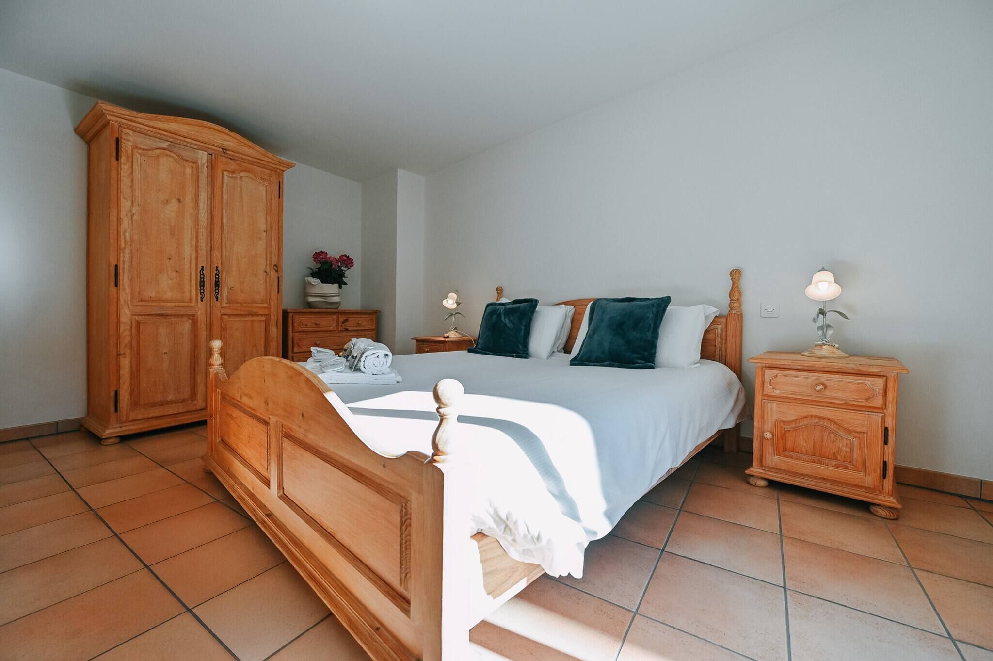 A bedroom with a wooden bed, a nightstand with a lamp, a wardrobe, and a dresser.
