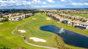 A golf course with bunkers, a pond, and residential buildings in the background. - Family-Friendly Home & Pool Near Disney (Davenport)