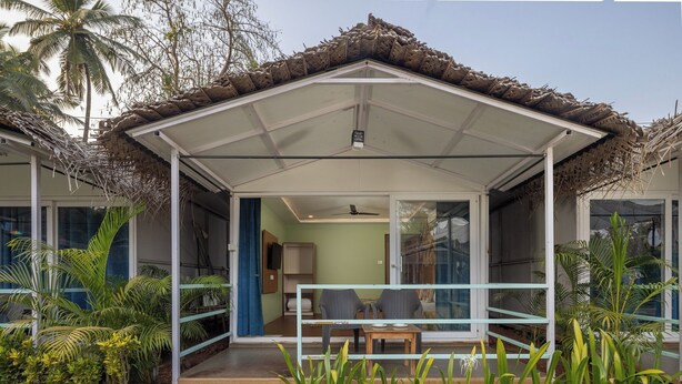 A covered outdoor area with a table and chairs, surrounded by plants and palm trees. - Palolem Casa (Canacona)