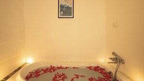 A bathtub with red rose petals, a framed picture on the wall, and a tiled floor. - Palolem Casa (Canacona)