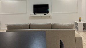 A modern living room with a flat-screen TV, a sofa, a coffee table, and a ceiling light fixture.