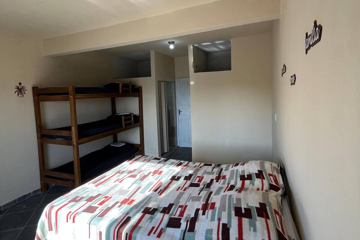 A room with a bunk bed, a patterned blanket, a tiled floor, and a door leading to another room.
