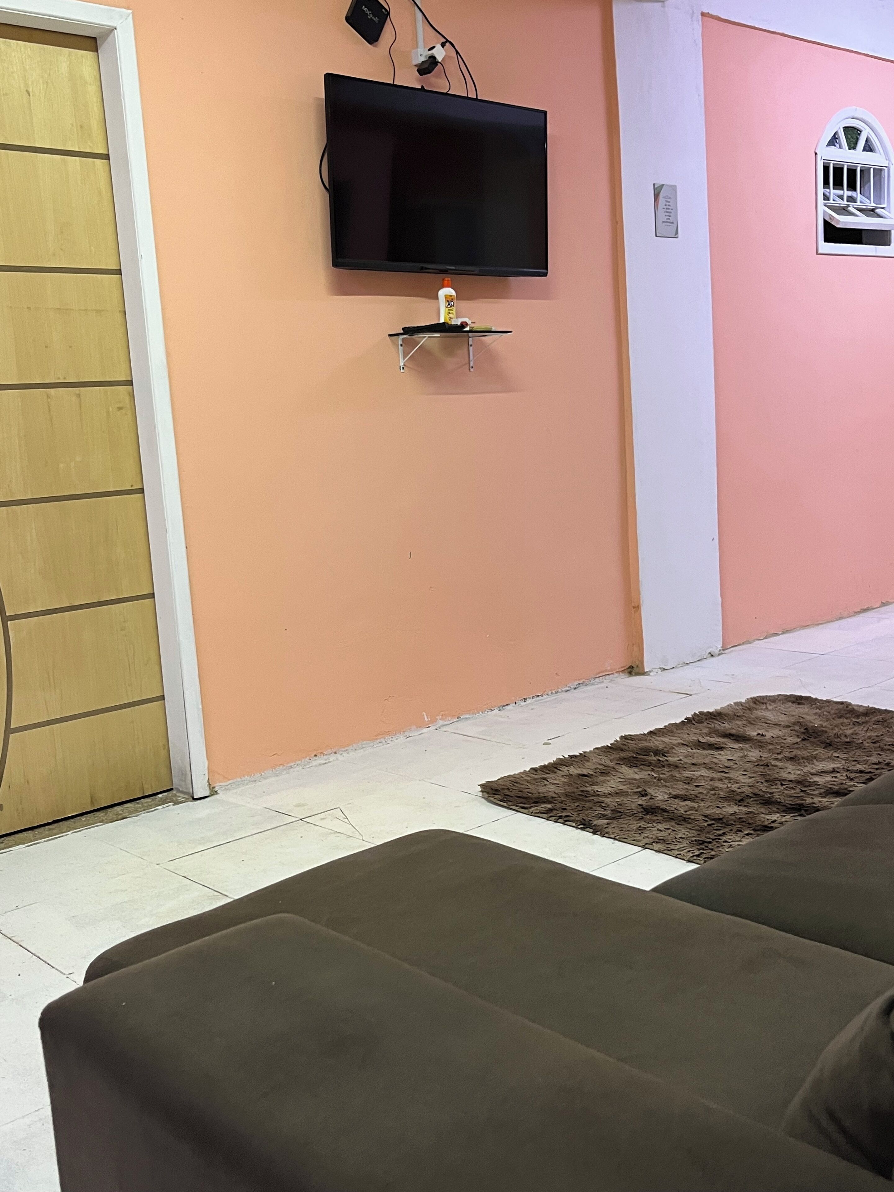 A room with a television mounted on the wall, a small shelf below it, and a brown sofa.