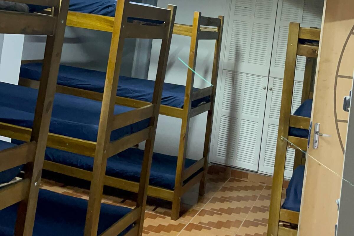 A dormitory room with bunk beds, a tiled floor, and a ceiling with fluorescent lighting.