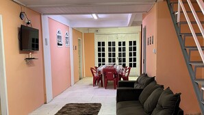Una sala de estar con sofá, televisor montado en la pared, mesa de comedor con sillas y una escalera.
