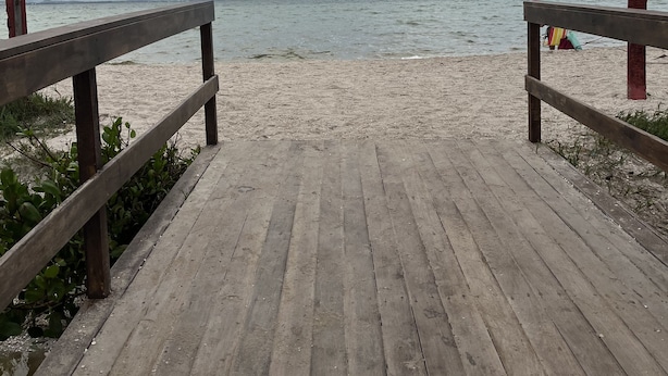 Un muelle de madera que conduce a una playa, con un cartel indicador a la derecha.