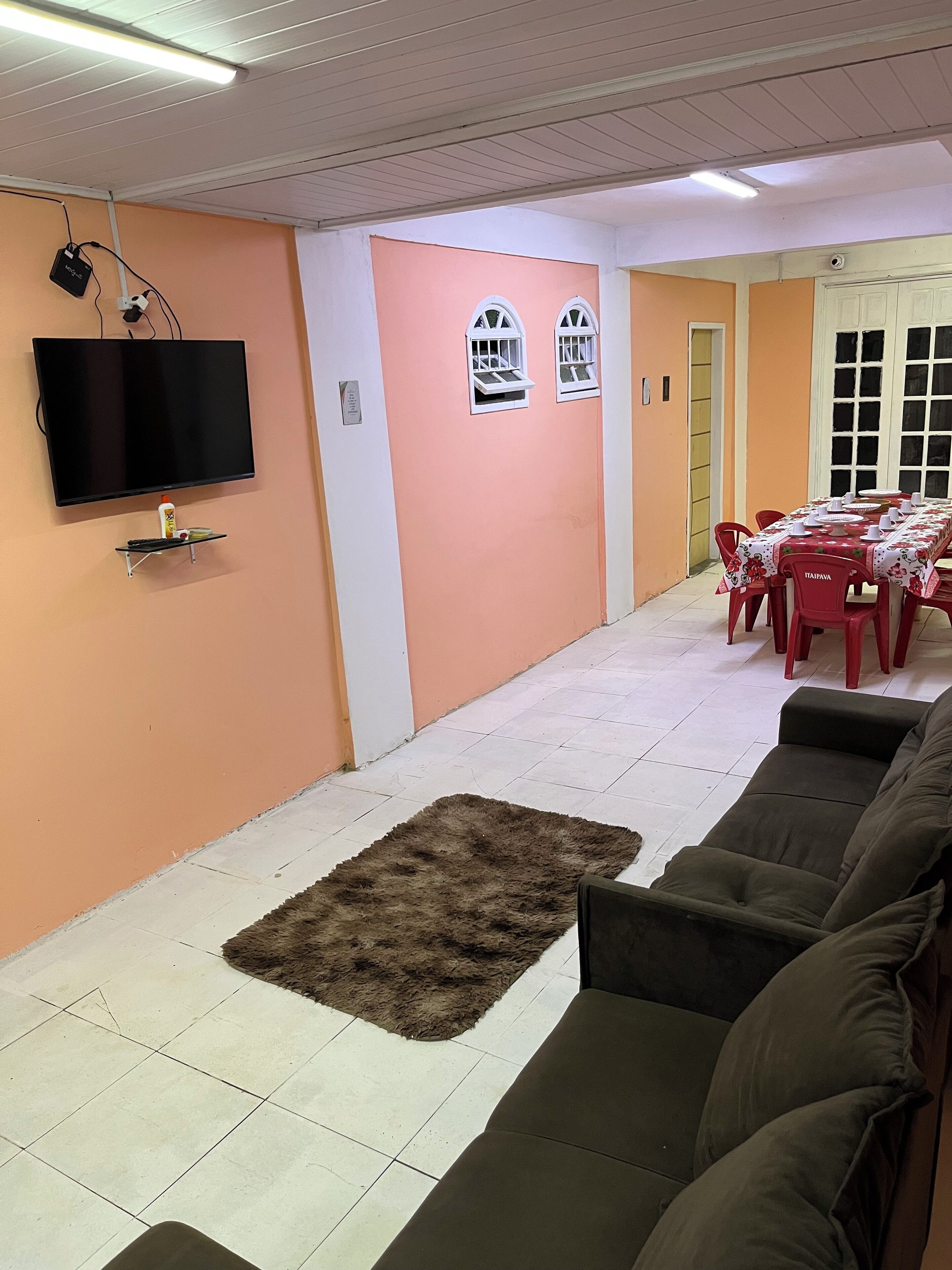 A living room with a flat-screen TV mounted on the wall, a small shelf with remote controls, a fluffy rug, and a sofa.