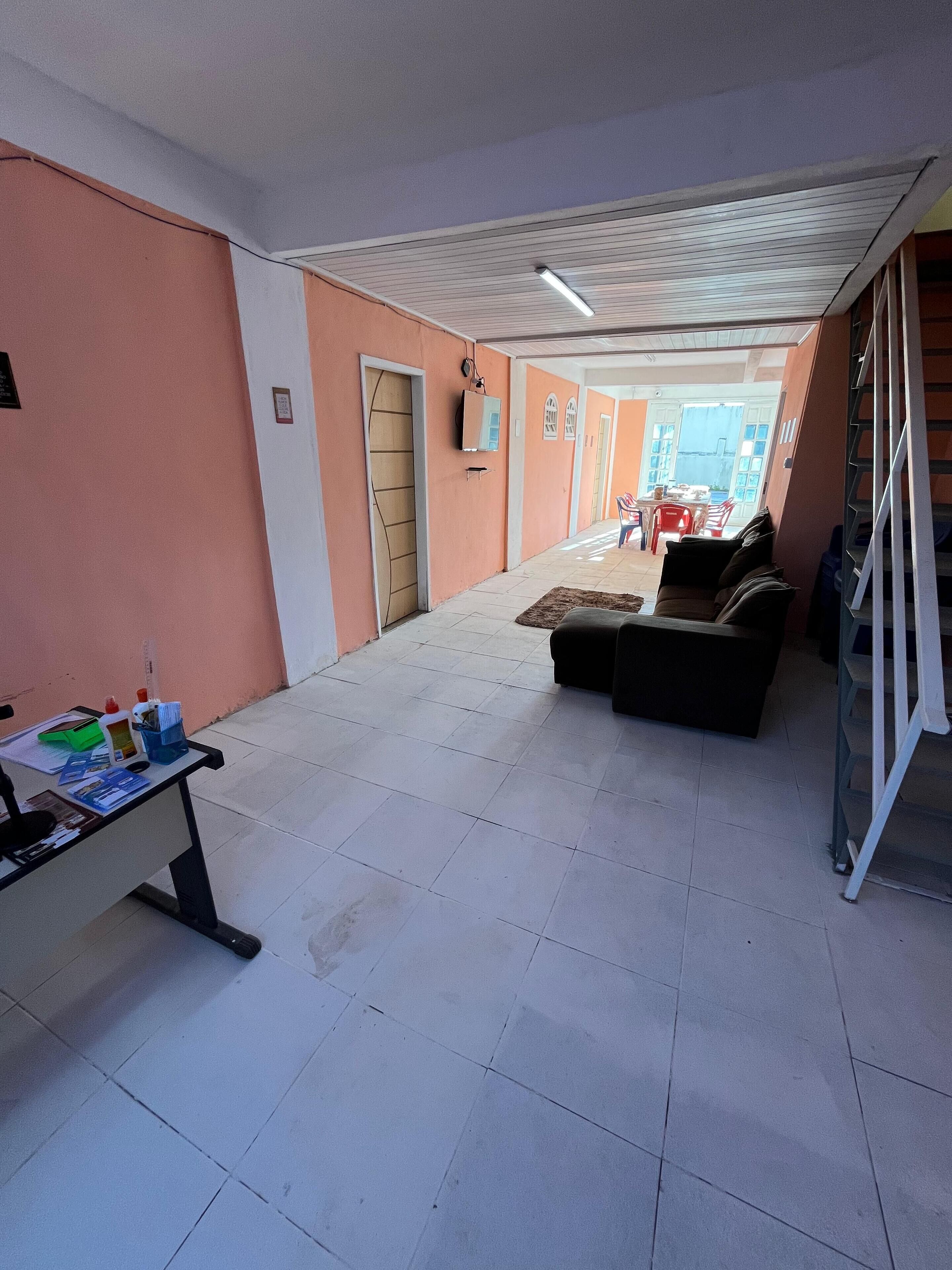 Un espacio interior amplio con suelo de baldosas, un sofá, un escritorio con material de oficina y una escalera.