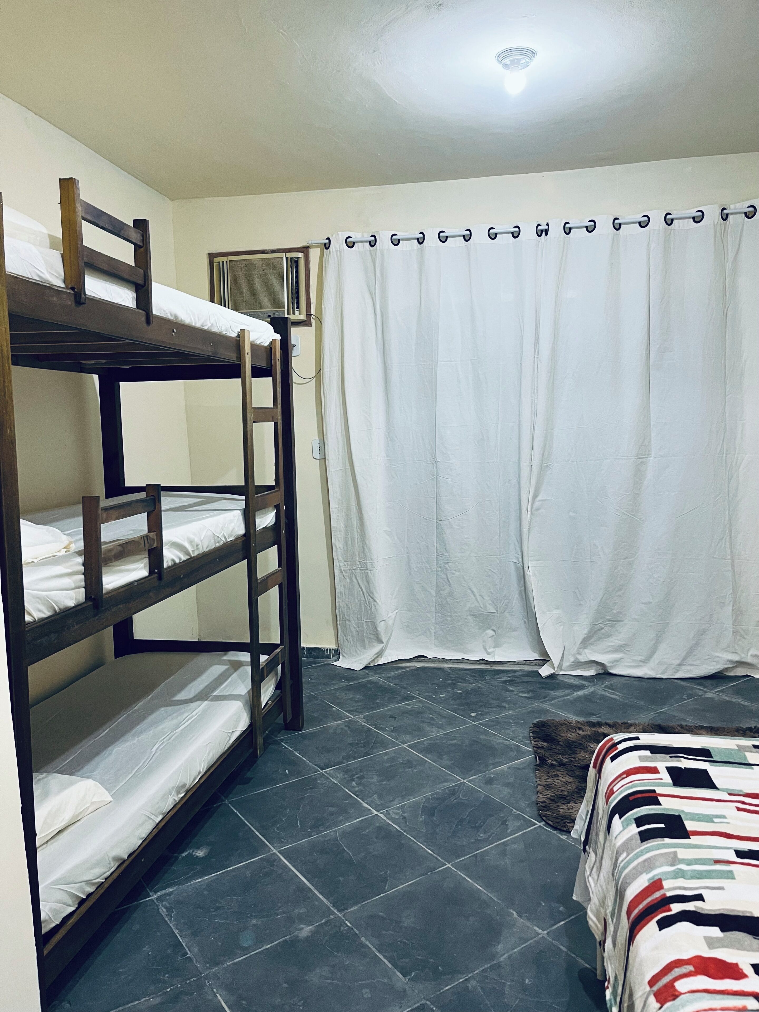 A dormitory room with bunk beds, a curtain, and a tiled floor.