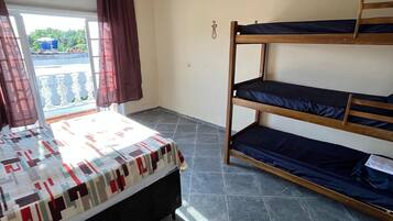 A room with a bed, a bunk bed, a window with curtains, and a view of greenery outside.