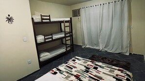 Un dormitorio con literas, una cama individual, una manta estampada, una cortina y una ventana pequeña.