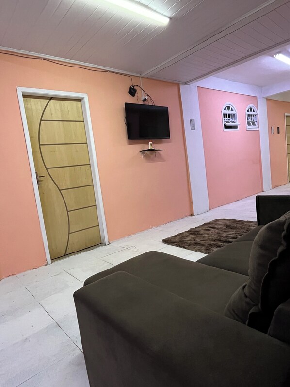 A room with a television mounted on the wall, a door with a unique design, and a small rug on the floor. - Hostel Sol do Alcaíra (Arraial do Cabo)