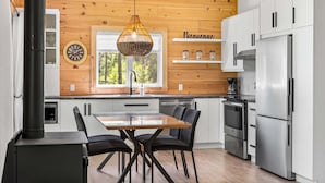 Een moderne keuken met houten wanden, een eettafel met stoelen, roestvrijstalen apparatuur en een bord met de tekst 'Bienvenue'.