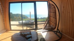 Un interior de madera con un amplio ventanal corredero que da a un balcón con vistas al mar y las colinas.