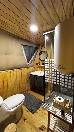 Ein kleines Badezimmer mit Holzvertäfelung, einer weißen Toilette, einem Waschbecken inklusive Spiegel und einer Duschkabine.