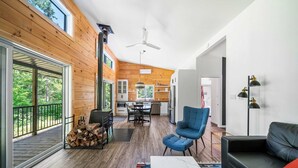 A spacious living area with a wooden floor, a blue armchair, a black sofa, and a dining table with chairs. - Spa, Nature & Riverside Escape | Ecureuil Roux (Trois-Rives)