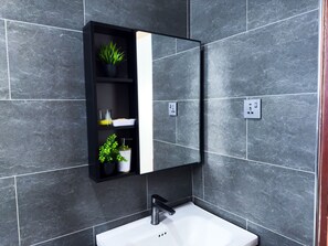 A bathroom with a black medicine cabinet, a white sink, and grey tiled walls.
