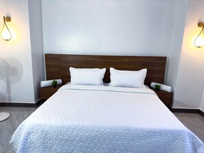 A neatly made bed with a wooden headboard, two bedside tables with lamps, and a wall-mounted fan.