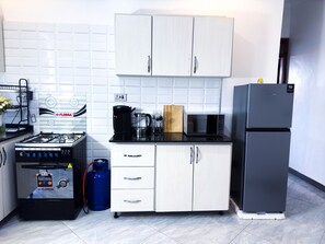 A compact kitchen with white cabinets, a gas stove, a microwave, and a refrigerator.