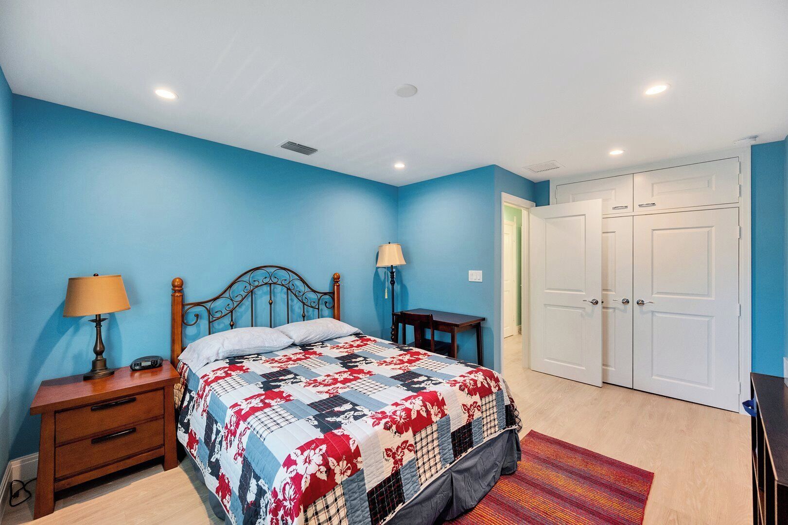 A bedroom with a bed, nightstands, a desk, and a wardrobe.