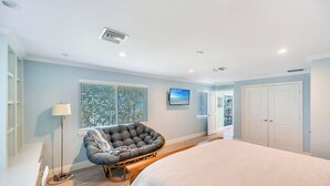 Une chambre avec un grand lit, une chaise, une télévision et une porte donnant sur un balcon.
