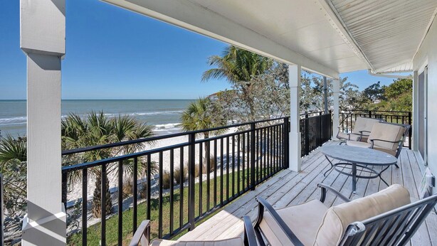 Un espace extérieur abrité, avec vue sur la plage, comprenant une table avec des chaises et une rambarde.
