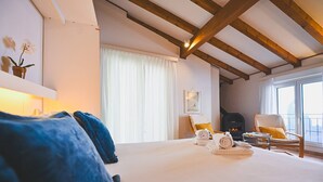 A bedroom with a large bed, a fireplace, a chair by the window, and a view of the outside. - Ruga Vacation Rental 7 in Ascona (Ascona)