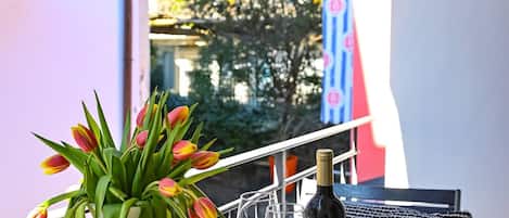 A balcony with a table set for two, featuring a vase of tulips and a bottle of wine.
