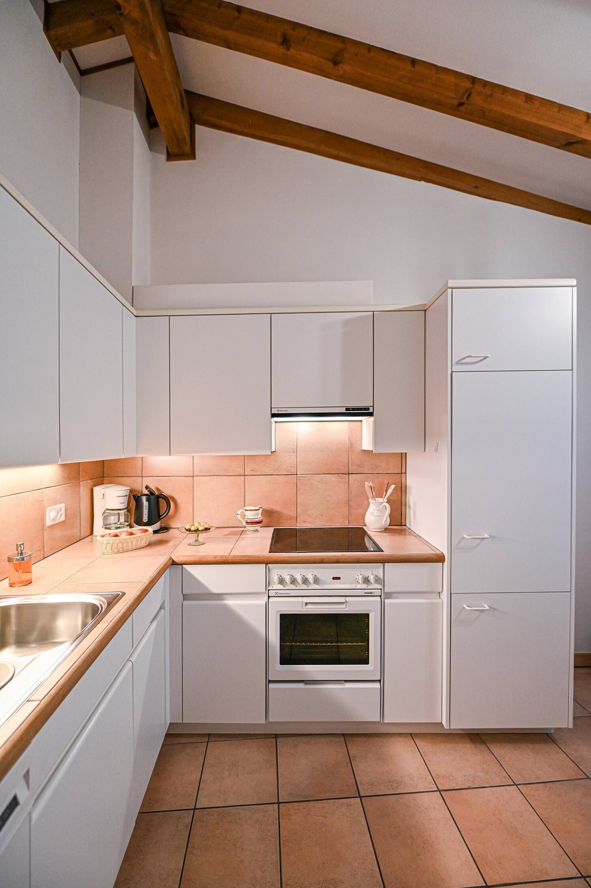 A compact kitchen with white cabinets, a built-in oven, and a stainless steel sink.