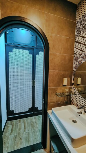 Casa de banho com lavatório branco, espelho e parede estampada.