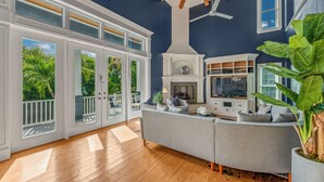A spacious living room with a large window, a fireplace, and a ceiling fan. - Castle Azul: Luxury canal front w/pool, hot tub, putting green, and ping pong (Anna Maria)