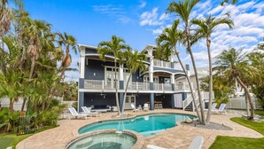 A two-story building with a pool, lounge chairs, and palm trees. - Castle Azul: Luxury canal front w/pool, hot tub, putting green, and ping pong (Anna Maria)