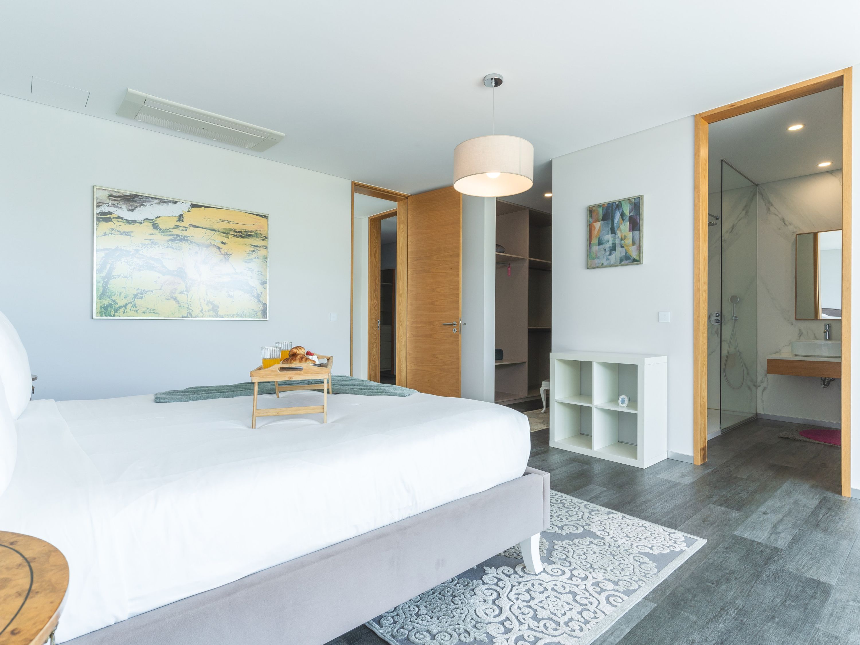 A modern bedroom with a large bed, bedside tables, a wardrobe, and a bathroom visible through an open door.