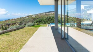 Uma casa moderna com varanda de vidro e vista para a paisagem costeira.