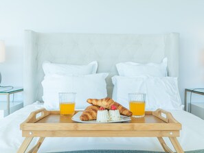 A bed with a wooden tray holding a croissant, two glasses of orange juice, and a plate with a pastry and raspberries. - Villa Primavera by Atlantic Holiday (Calheta)