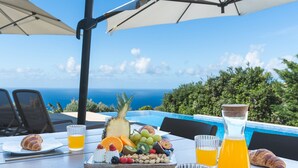 Disposição para o café da manhã com croissants, frutas, nozes e suco de laranja em uma mesa com vista para a piscina.