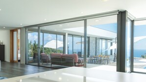 Um interior moderno com uma grande porta de vidro que dá para uma varanda com área de estar e vista para o oceano.