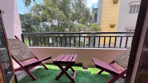 A balcony with three wooden lounge chairs and a small table, surrounded by artificial green grass. - Soloscape budget friendly backpackers hostel (Bengaluru)