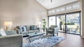 Un vaste salon doté d’une grande porte vitrée donnant sur un patio. On y trouve deux canapés, une table basse et une lampe.