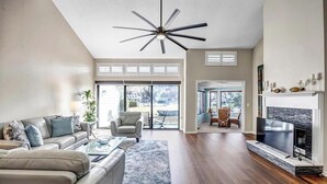 Un salon spacieux doté d’un ventilateur de plafond moderne, d’une cheminée et d’un grand téléviseur.