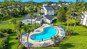 Un quartier résidentiel doté d’une piscine, entouré de palmiers et de maisons.